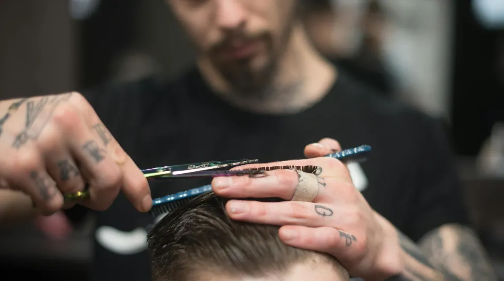 Detail rukou barbera při precizním střihu vlasů nůžkami v barbershopu.