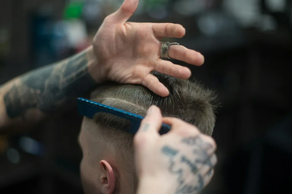 Barber stříhá vlasy klientovi nůžkami v barbershopu