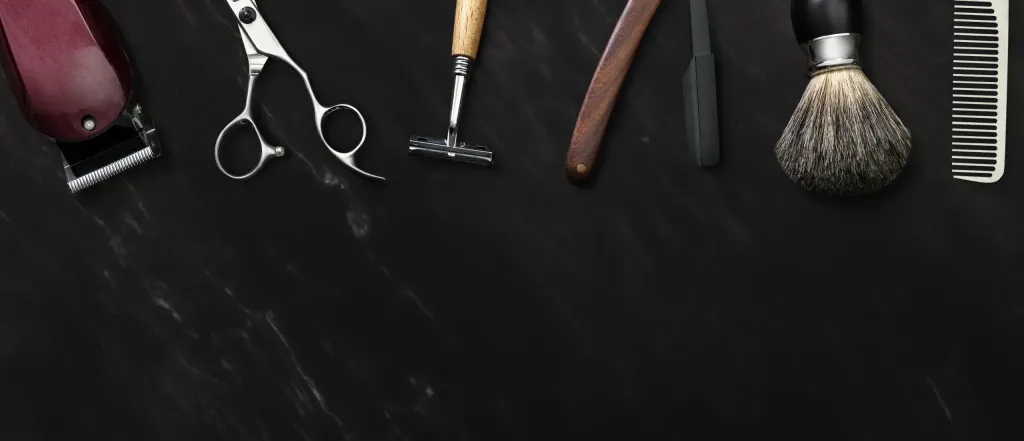 Nástroje barbera na černém mramorovém pozadí — strojek, nůžky, břitva, holicí štětec a hřeben